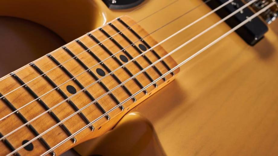 The image shows a view of the guitar fretboard of a Fender Stratocaster from a distance, highlighting the entire fretboard with visible fret markers and the six strings, including the low E string and high E string. This perspective allows guitar students to see the arrangement of notes on the fretboard, including open strings and various frets, useful for learning chords and individual notes.